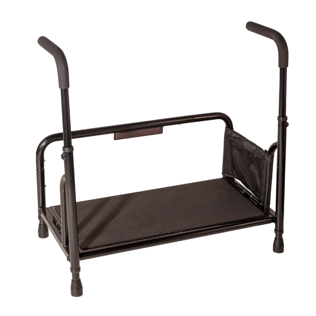 The Stander Step Bedside Platform with LED Lighting is a black metal assist rail featuring two padded handles, a flat support platform, adjustable legs, mesh side pocket, safety step, and built-in LED lights for safe bed entry and exit.